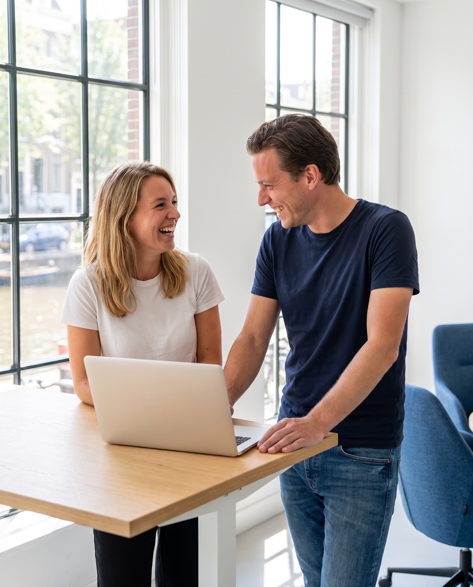 Two colleagues laughing together over a laptop at the Véora Group office